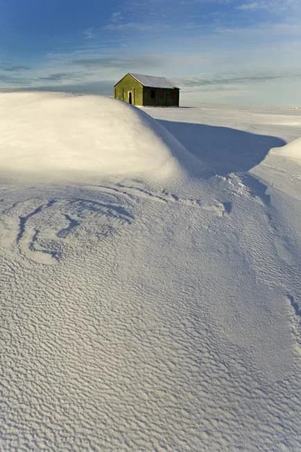 Einmana snævi þakinn skúr undir vetrarhimni